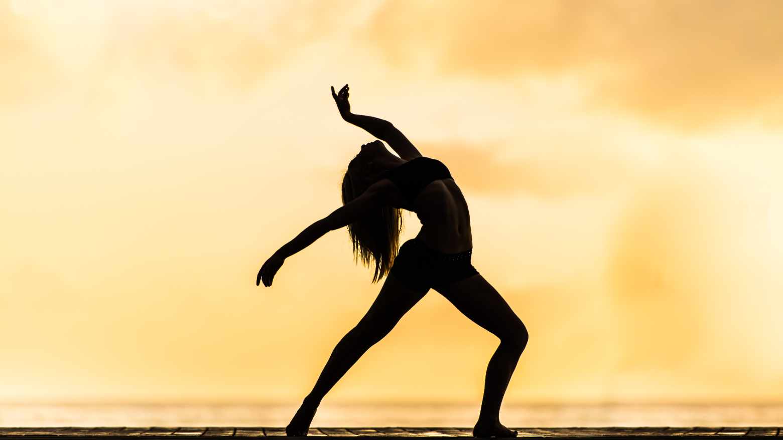 A woman doing a yoga pose on the beach at sunset. 
