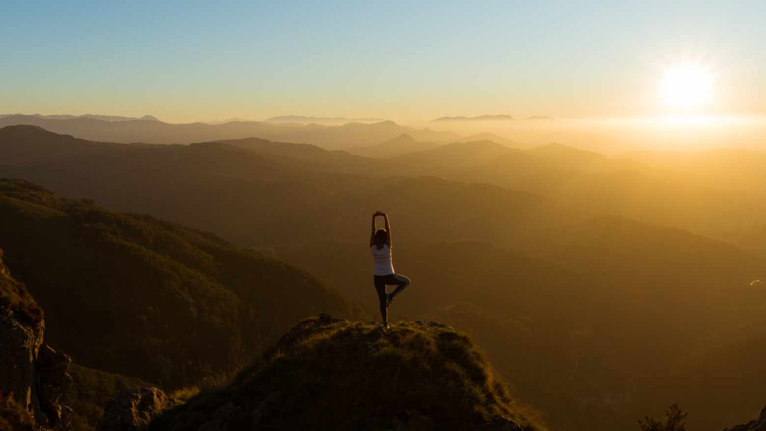 A woman doing a yoga pose on a mountain during sunrise. 