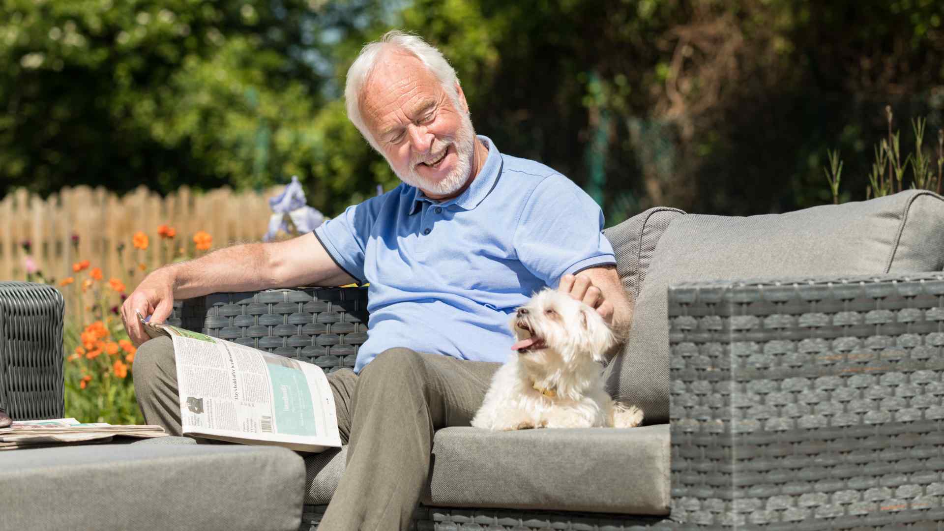 A man sitting with a dog on a garden sofa on a sunny day.