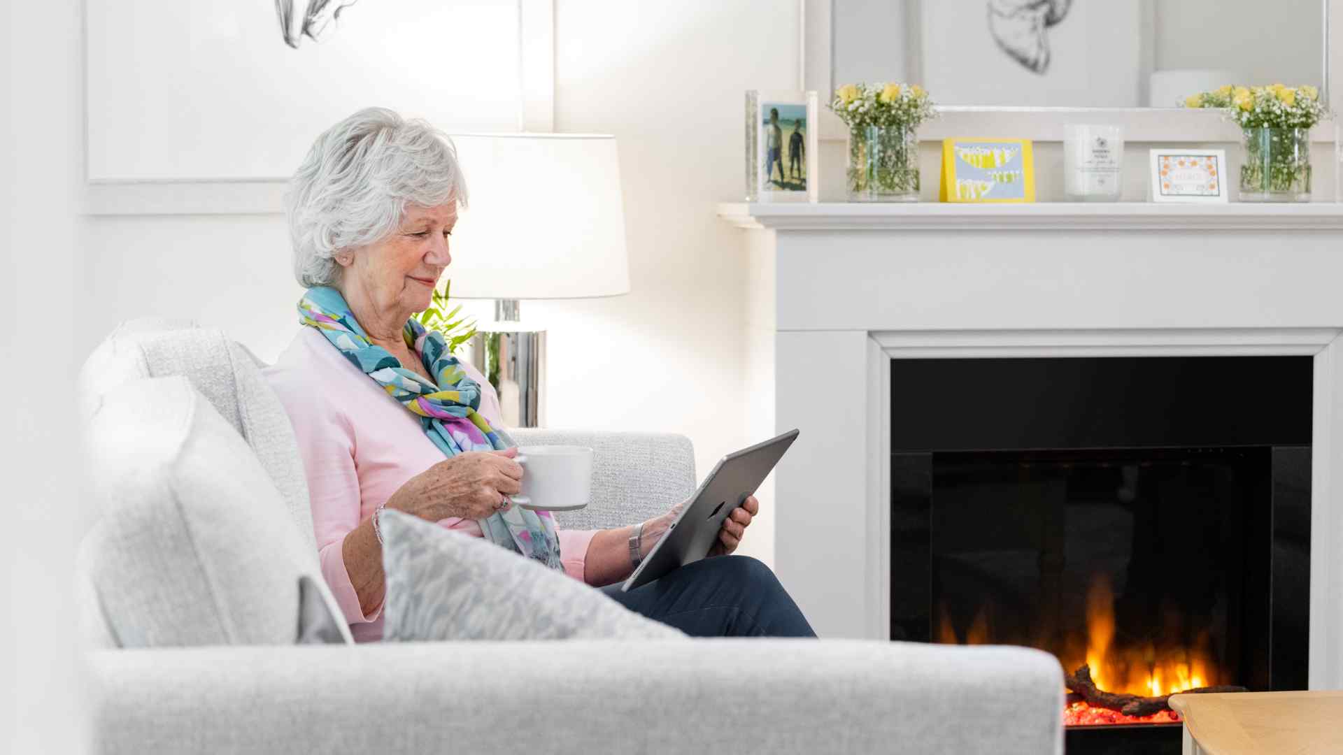 A lady using an iPad while sat next to a fire place in her drawing room