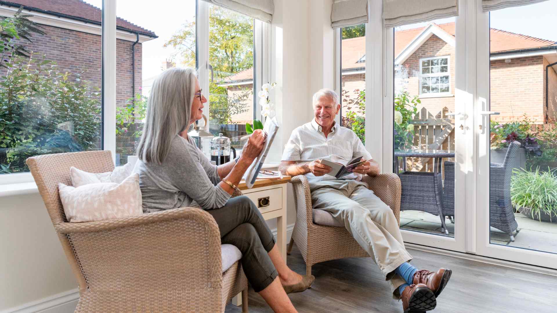 A man and wife relaxing in the sunroom doing the crossword and reading a book on a sunny day.