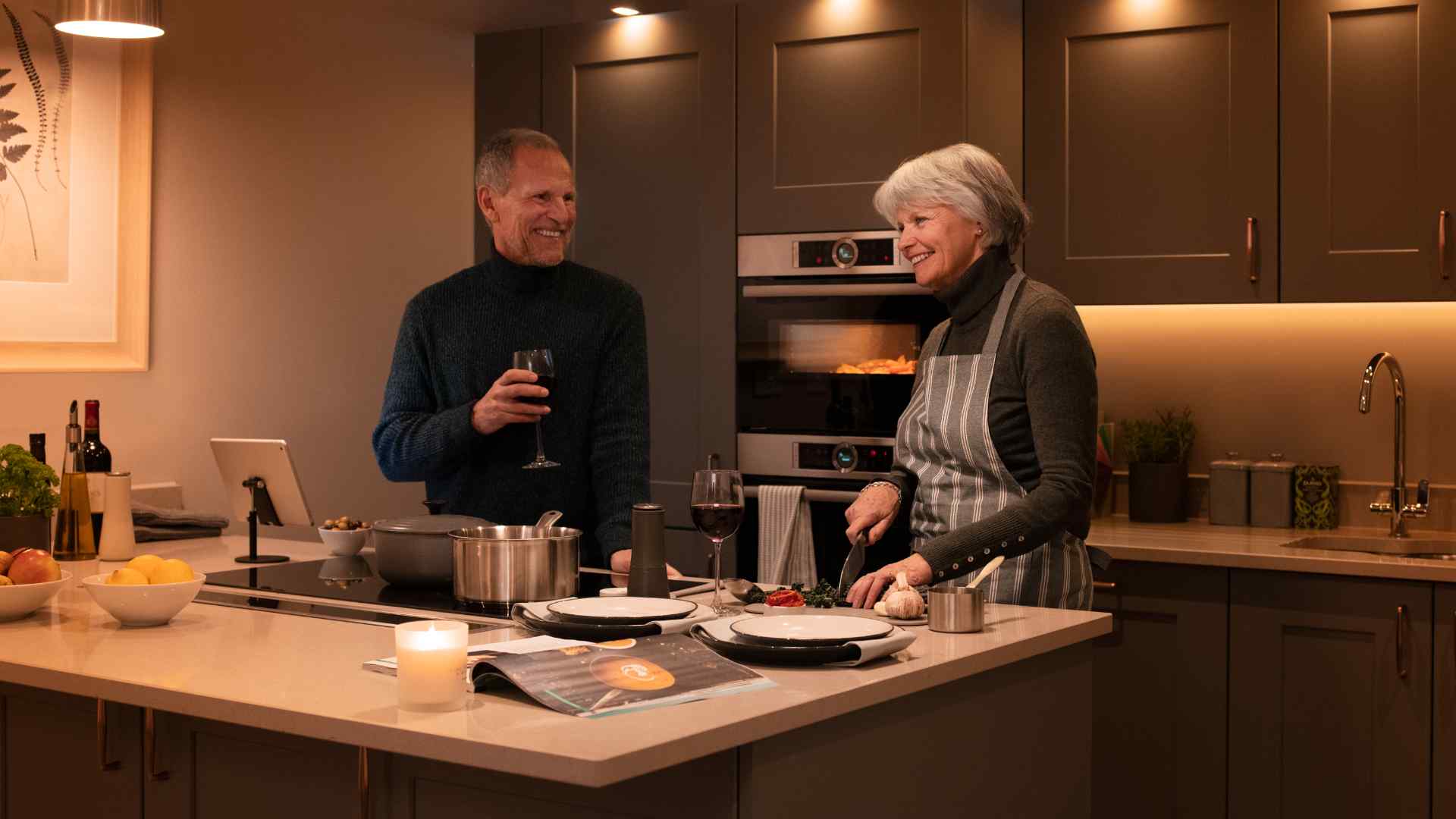 A husband and wife in a dark kitchen cooking a meal together.