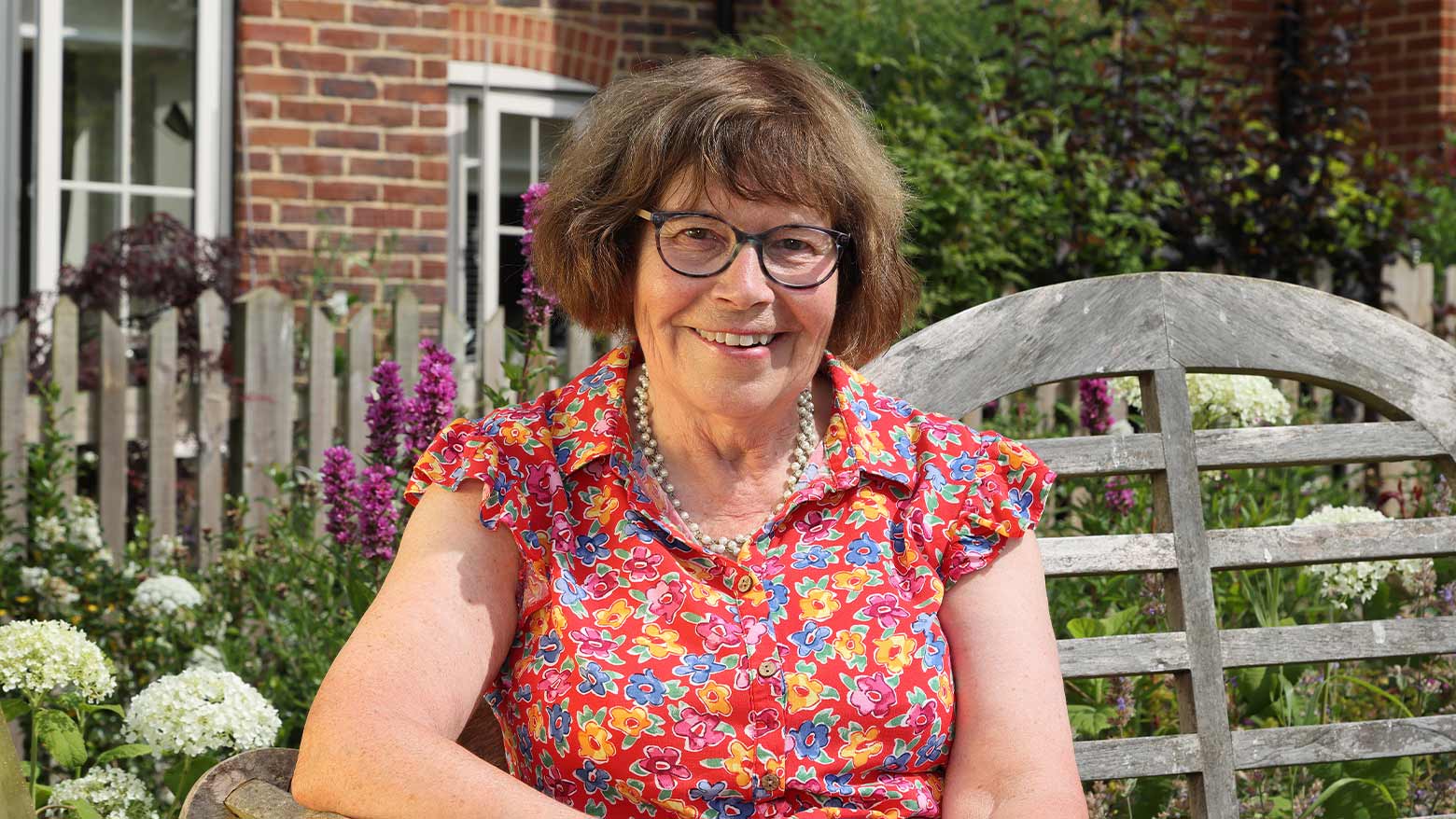 Mrs Markham on a garden bench in a flowery top 