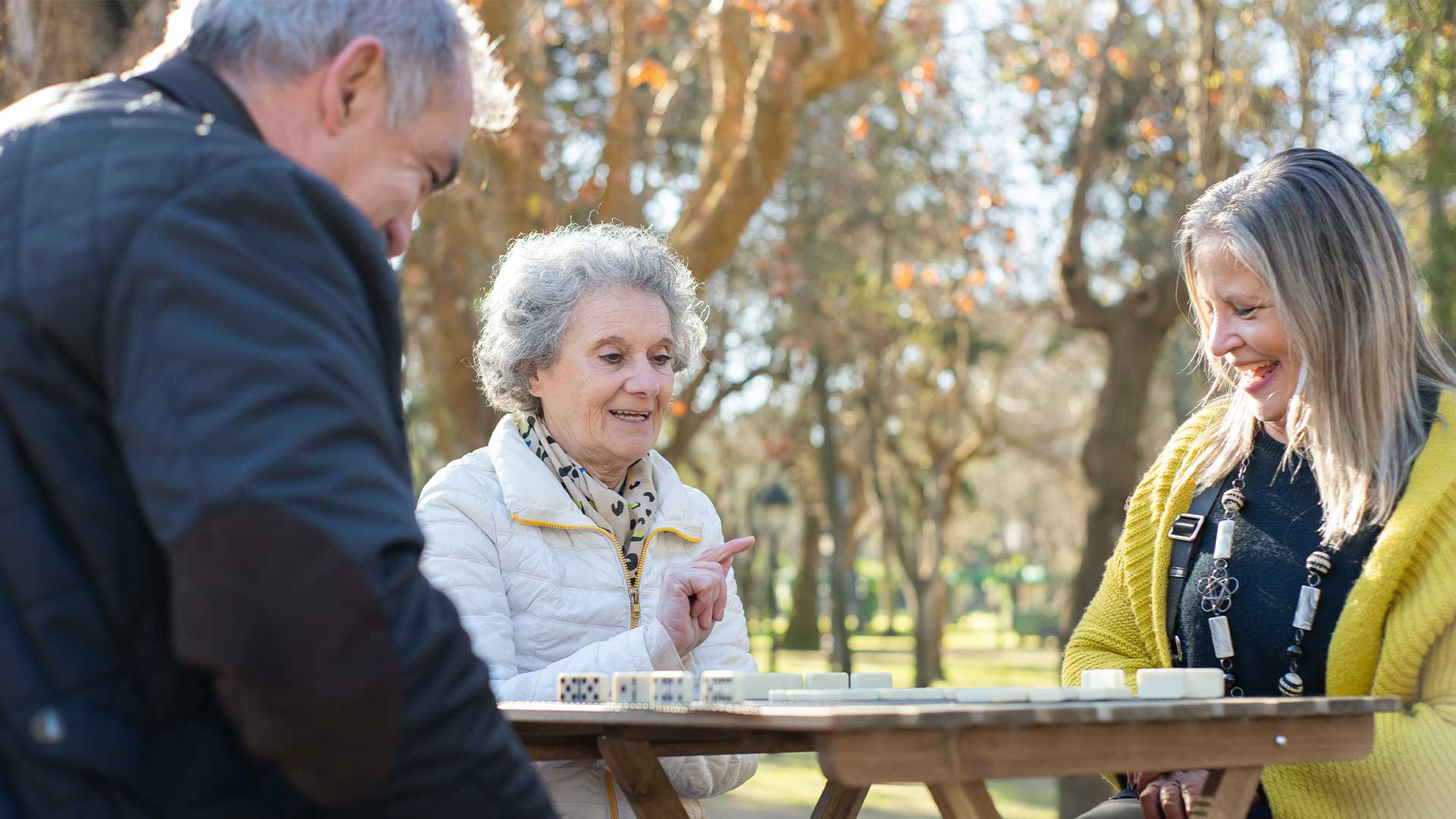 Three elderly people playing a board game outside. 