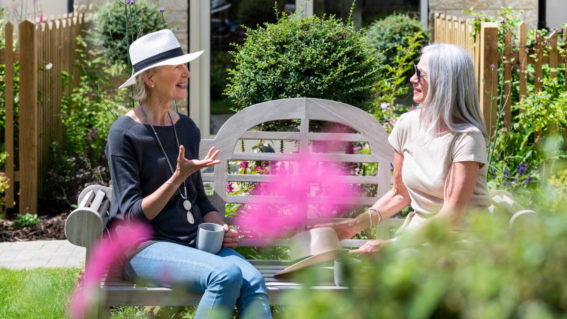 Two ladies talking whilst sat outside on a bench.