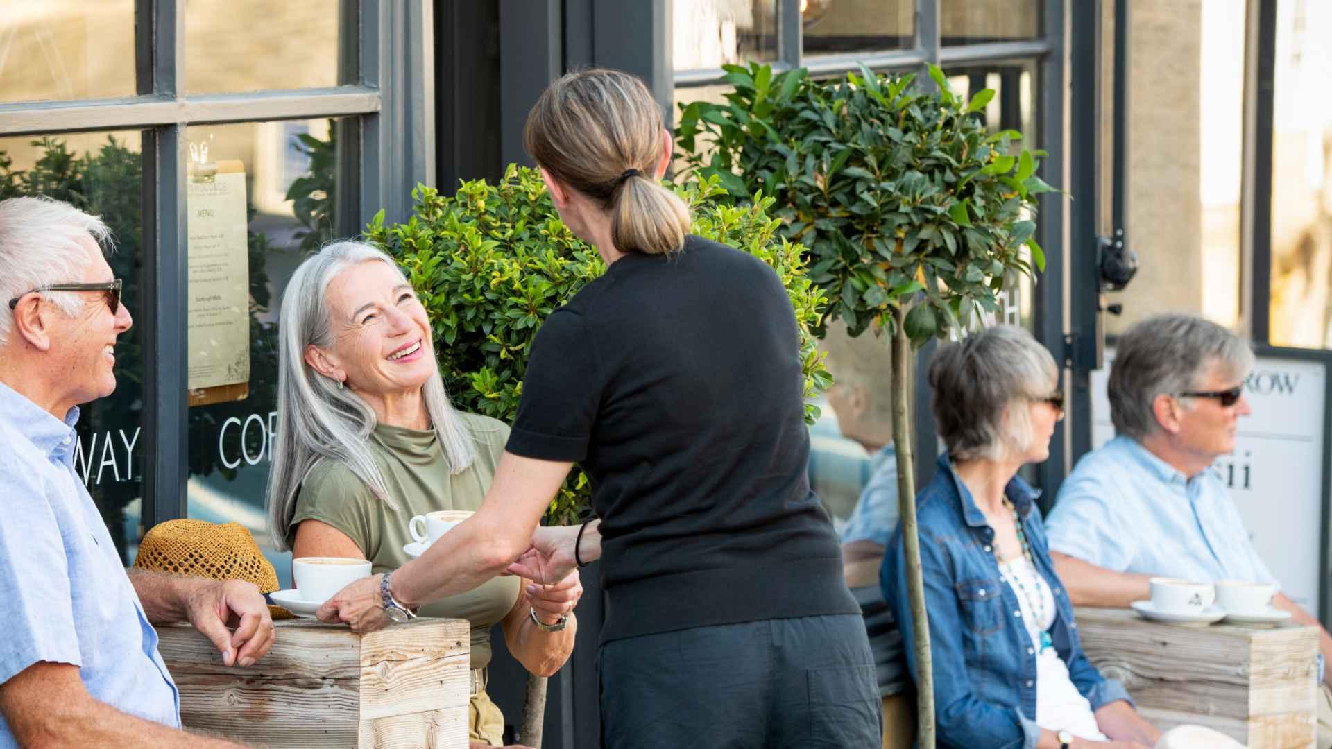 A lady being served coffee by a waitress in a black in Burford. 
