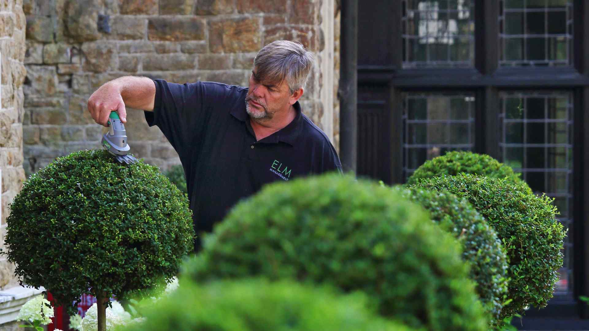 An estate manager trimming a bush at a development